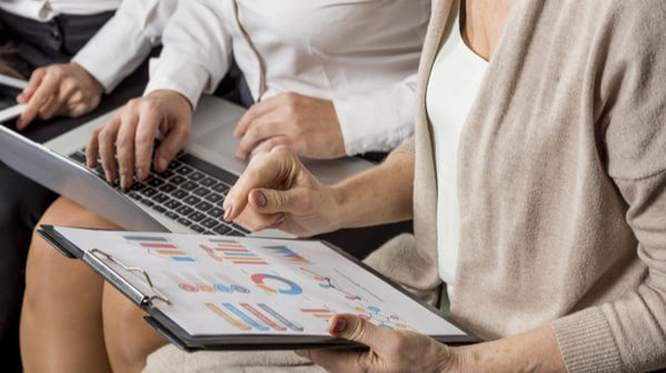 Pessoas analisando gráficos de investimentos em prancheta e laptop durante reunião de gestão de carteiras para RPPS.