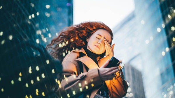 Mulher com expressão de preocupação olhando o celular em meio a prédios iluminados, simbolizando o impacto da comparação social e das pressões financeiras no comportamento financeiro.