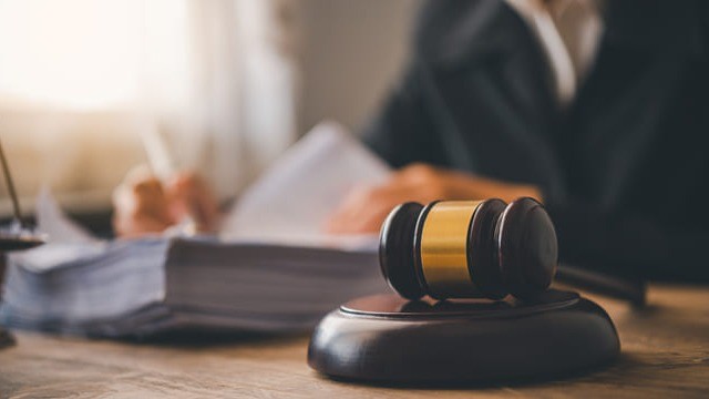 Martelo de juiz sobre a mesa, com pessoa ao fundo revisando documentos jurídicos, representando decisão judicial sobre CRP e fiscalização dos Regimes Próprios de Previdência Social (RPPS).